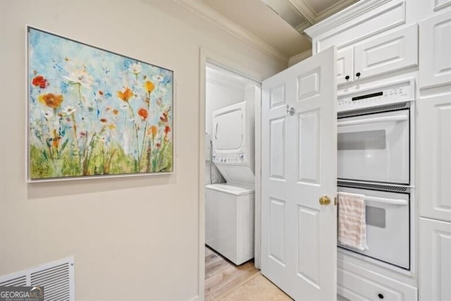 kitchen with white cabinetry, white double oven, ornamental molding, stacked washer and clothes dryer, and light hardwood / wood-style flooring