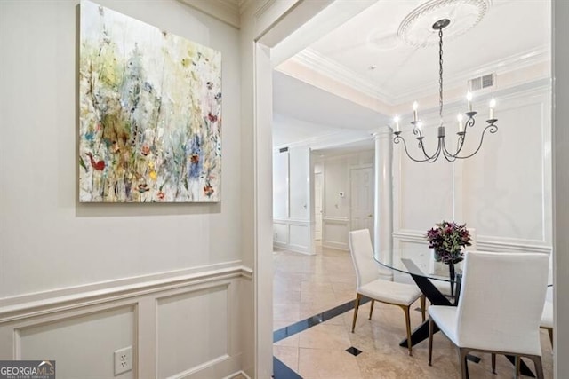 dining room with a raised ceiling, ornamental molding, a chandelier, and ornate columns