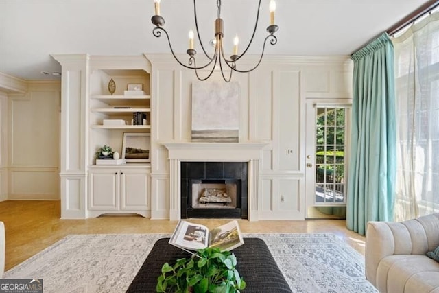 living room featuring an inviting chandelier, crown molding, built in features, and a tile fireplace