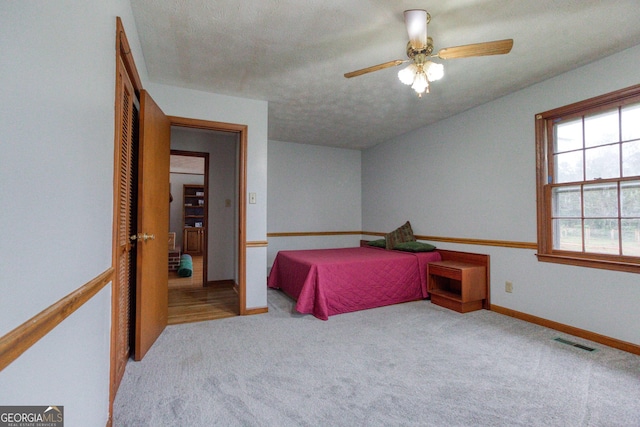 bedroom featuring ceiling fan, light colored carpet, and a textured ceiling