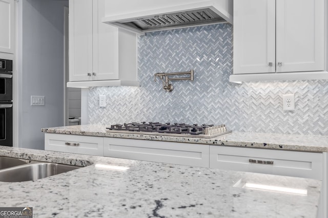 kitchen featuring premium range hood, light stone counters, tasteful backsplash, white cabinets, and stainless steel gas stovetop