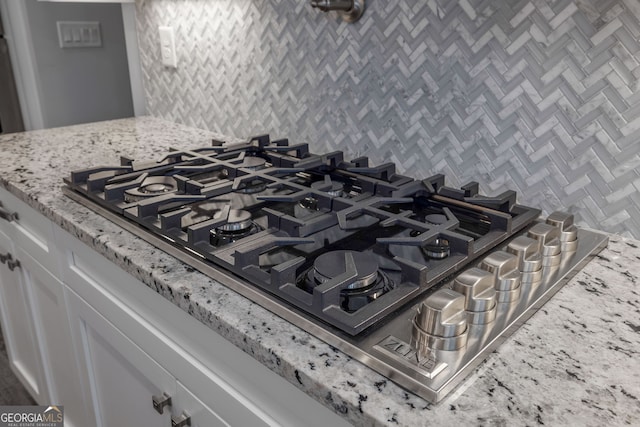 room details featuring stainless steel gas stovetop, light stone countertops, and white cabinets