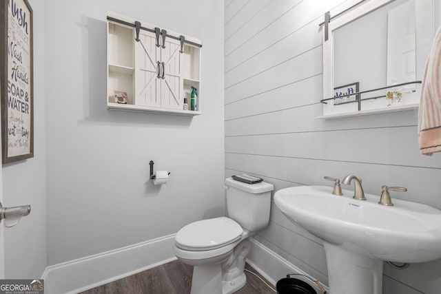 bathroom with sink, toilet, hardwood / wood-style floors, and wood walls