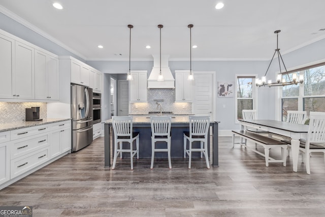 kitchen featuring appliances with stainless steel finishes, white cabinetry, hanging light fixtures, light stone countertops, and custom range hood