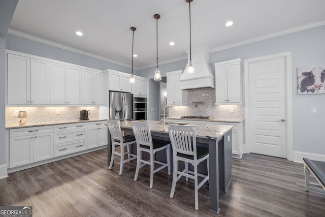 kitchen with appliances with stainless steel finishes, white cabinetry, hanging light fixtures, a kitchen island with sink, and light stone countertops