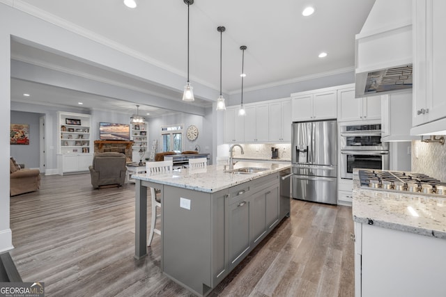 kitchen with appliances with stainless steel finishes, pendant lighting, white cabinetry, an island with sink, and sink