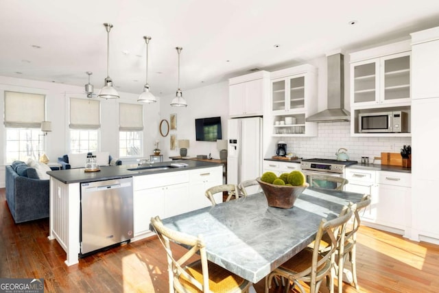 kitchen with appliances with stainless steel finishes, white cabinetry, sink, hanging light fixtures, and wall chimney exhaust hood