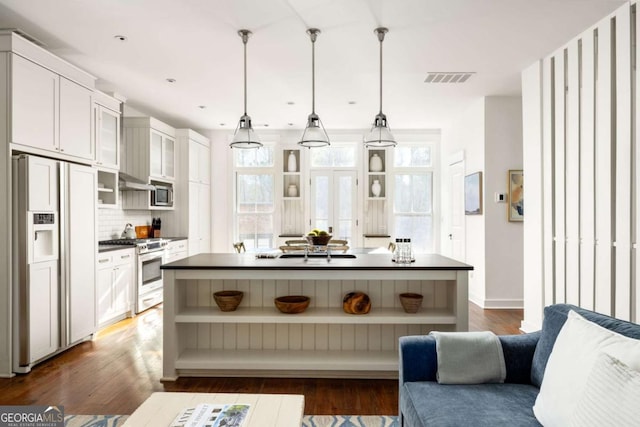 kitchen featuring a kitchen island, appliances with stainless steel finishes, decorative light fixtures, tasteful backsplash, and white cabinetry