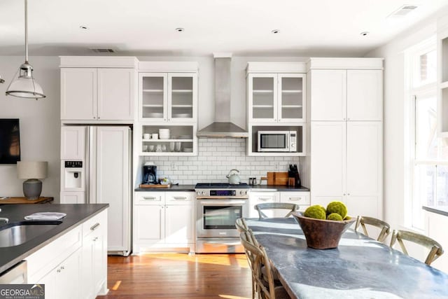 kitchen with white cabinetry, hanging light fixtures, paneled built in refrigerator, stainless steel range, and wall chimney range hood