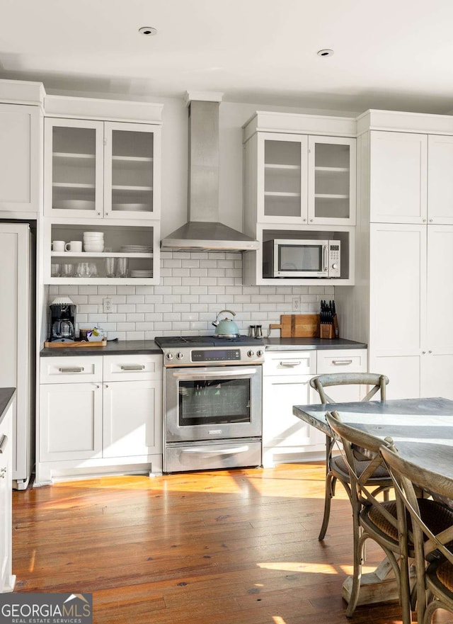 kitchen featuring tasteful backsplash, white cabinets, stainless steel appliances, and wall chimney range hood