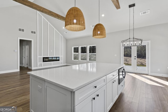 kitchen with pendant lighting, beamed ceiling, white cabinetry, dark hardwood / wood-style flooring, and a center island