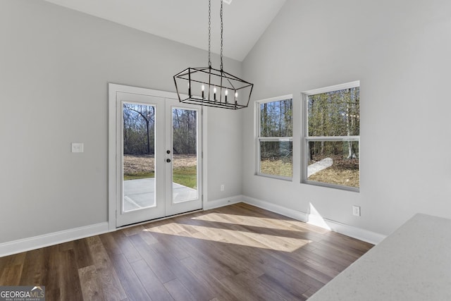 unfurnished dining area with hardwood / wood-style floors, a notable chandelier, high vaulted ceiling, and french doors