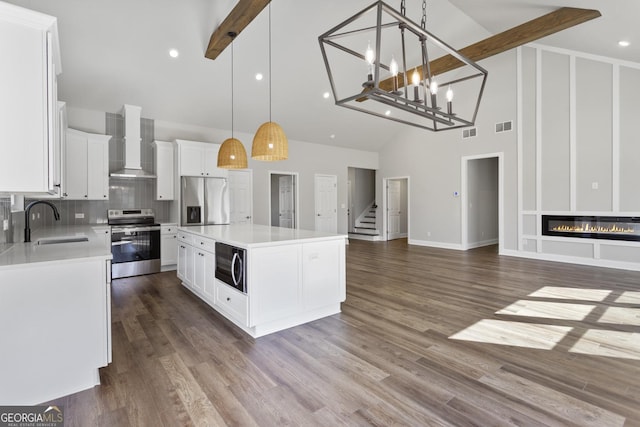 kitchen with appliances with stainless steel finishes, a kitchen island, decorative light fixtures, sink, and wall chimney exhaust hood