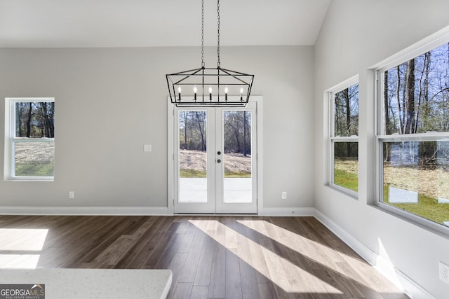 unfurnished dining area with vaulted ceiling, a notable chandelier, dark hardwood / wood-style flooring, and french doors