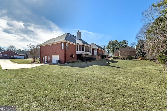 view of side of home with a chimney, an attached garage, a yard, brick siding, and a sunroom