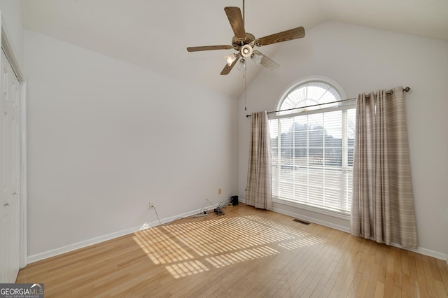 spare room featuring lofted ceiling, hardwood / wood-style flooring, visible vents, baseboards, and a ceiling fan