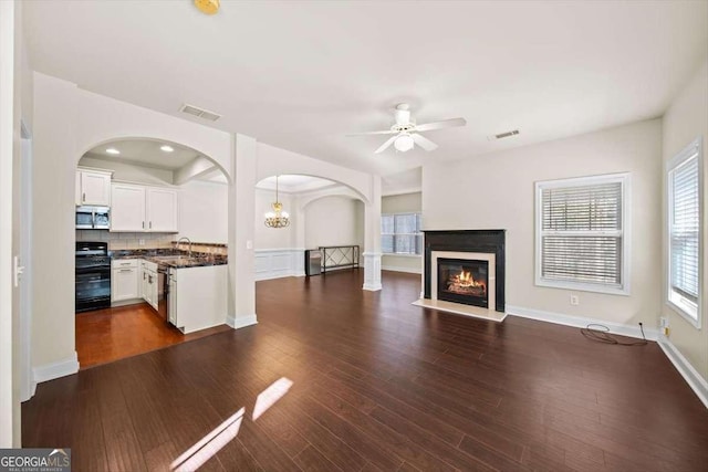 unfurnished living room featuring ceiling fan with notable chandelier, dark hardwood / wood-style floors, and sink