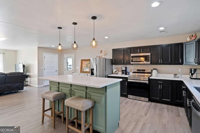 kitchen with a kitchen bar, hanging light fixtures, appliances with stainless steel finishes, a kitchen island, and light hardwood / wood-style floors