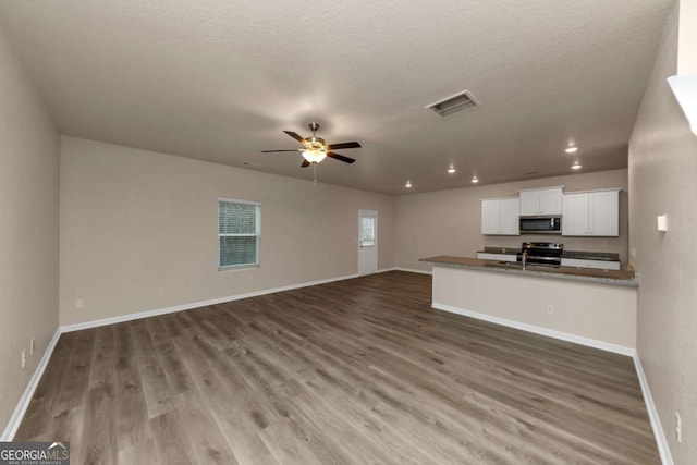 unfurnished living room with a textured ceiling, dark wood-type flooring, and ceiling fan