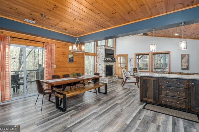 dining area featuring wood ceiling, hardwood / wood-style flooring, wooden walls, a stone fireplace, and vaulted ceiling