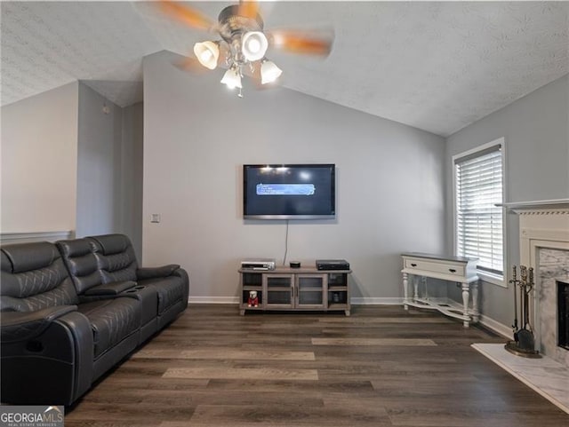 living room featuring dark wood-type flooring, ceiling fan, a fireplace, and vaulted ceiling