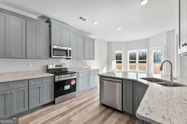 kitchen with light stone counters, sink, gray cabinetry, and appliances with stainless steel finishes