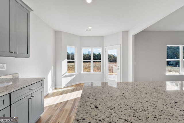 kitchen featuring gray cabinets, light stone countertops, a healthy amount of sunlight, and light wood-type flooring