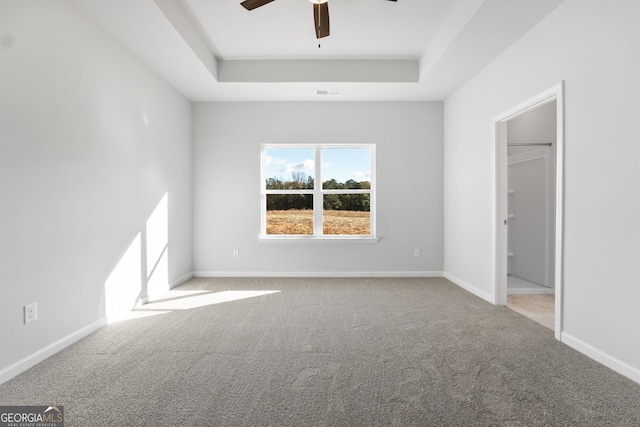 unfurnished bedroom featuring a walk in closet, light carpet, ceiling fan, and a tray ceiling