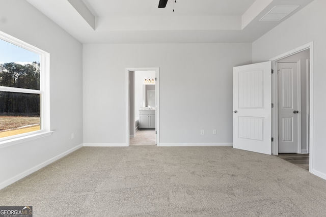 unfurnished bedroom featuring ensuite bath, a raised ceiling, carpet floors, and multiple windows