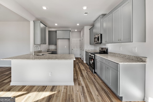 kitchen with sink, gray cabinetry, appliances with stainless steel finishes, dark hardwood / wood-style flooring, and light stone countertops