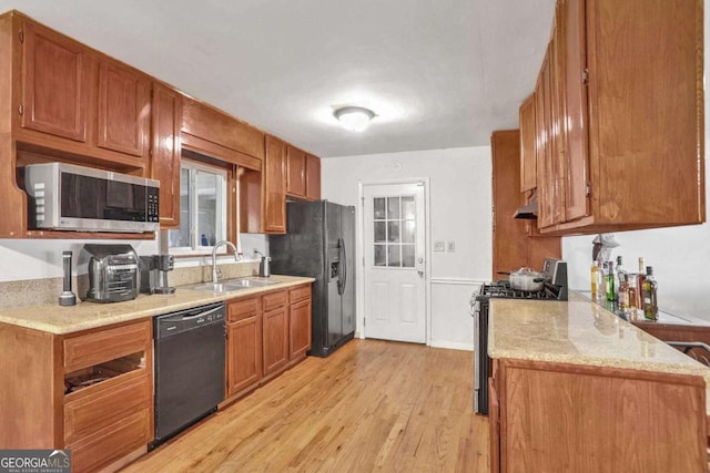 kitchen with sink, black appliances, light stone countertops, and light wood-type flooring