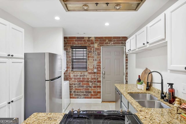 kitchen with stainless steel appliances, white cabinetry, brick wall, and sink