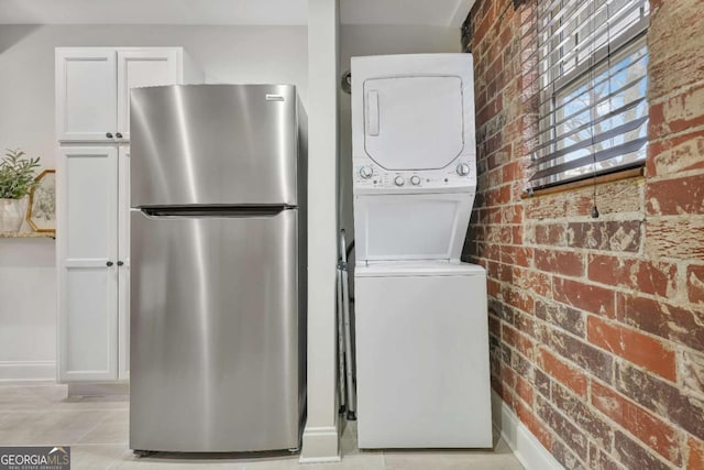 washroom featuring light tile patterned flooring, brick wall, and stacked washer / drying machine