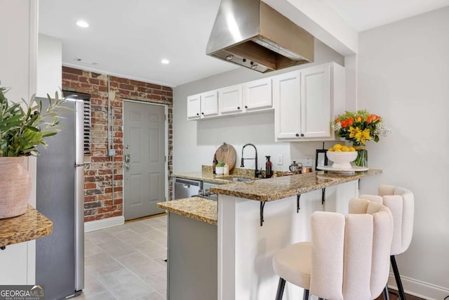 kitchen featuring a breakfast bar, light stone counters, appliances with stainless steel finishes, kitchen peninsula, and brick wall