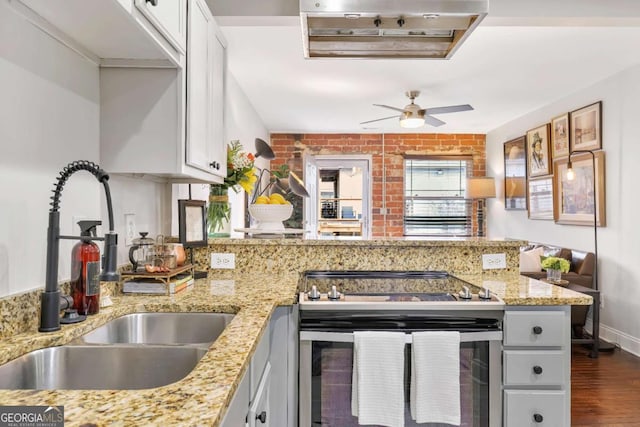 kitchen with sink, stainless steel range with electric cooktop, white cabinetry, light stone counters, and kitchen peninsula