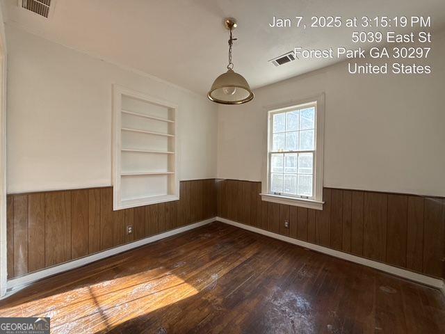 empty room featuring wooden walls, built in features, and dark hardwood / wood-style floors