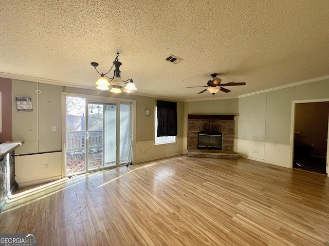 unfurnished living room with crown molding, ceiling fan with notable chandelier, light hardwood / wood-style floors, a textured ceiling, and a stone fireplace