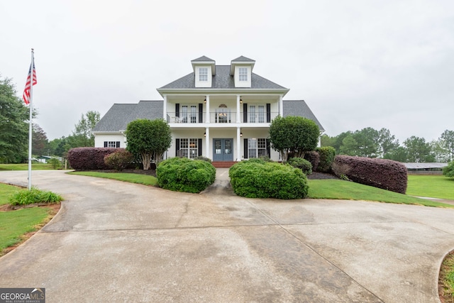 view of front of house featuring a front lawn, french doors, a balcony, and covered porch