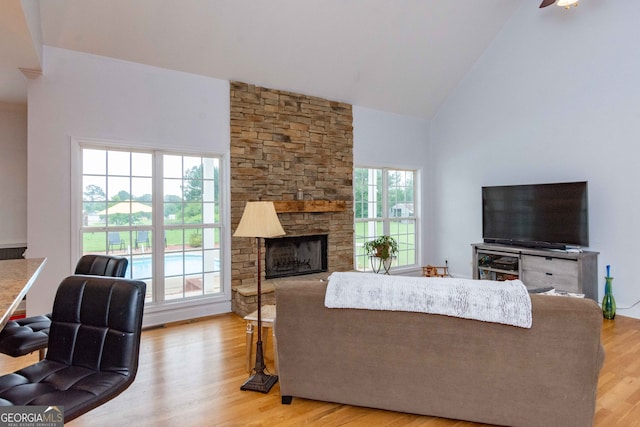 living room with a stone fireplace, high vaulted ceiling, and light hardwood / wood-style floors