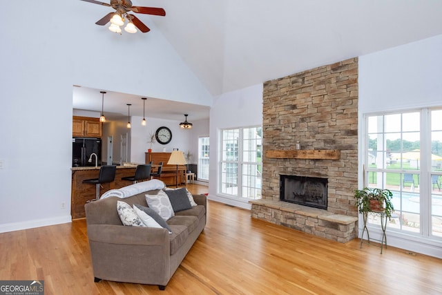 living room featuring a stone fireplace, plenty of natural light, high vaulted ceiling, and light wood-type flooring