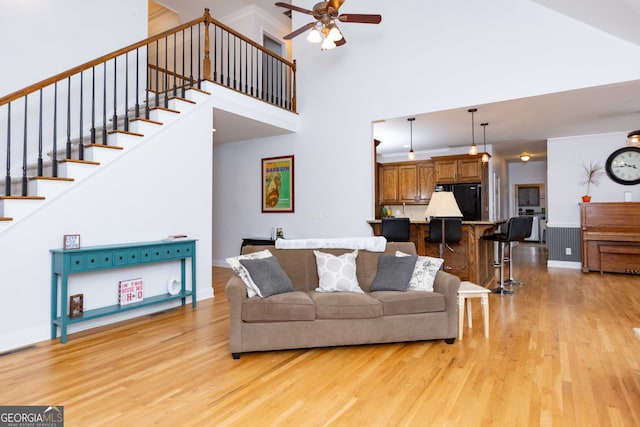 living room with a high ceiling, ceiling fan, and light hardwood / wood-style flooring