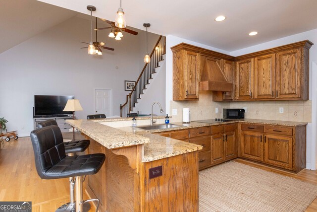 kitchen with wall chimney exhaust hood, a breakfast bar, sink, kitchen peninsula, and black appliances