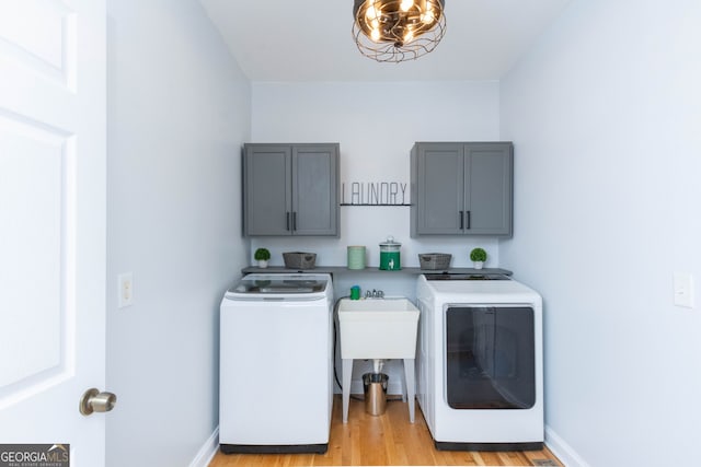 clothes washing area featuring cabinets, separate washer and dryer, a notable chandelier, and light hardwood / wood-style flooring