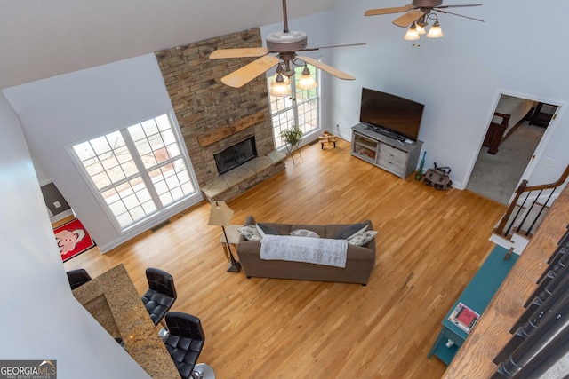 living room with hardwood / wood-style flooring, ceiling fan, a stone fireplace, and high vaulted ceiling