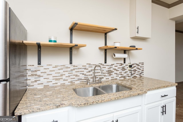 kitchen with light stone counters, sink, stainless steel refrigerator, and white cabinets