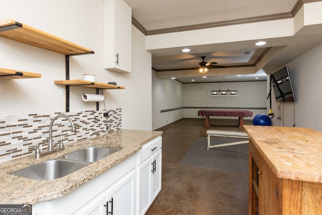 kitchen with sink, white cabinetry, backsplash, light stone counters, and ornamental molding