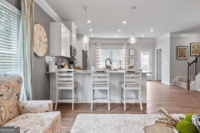 kitchen featuring a kitchen bar, pendant lighting, stainless steel appliances, light stone countertops, and white cabinets