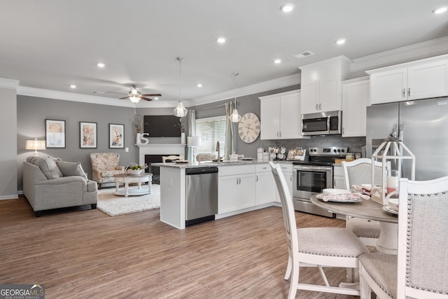 kitchen with pendant lighting, wood-type flooring, sink, white cabinets, and stainless steel appliances