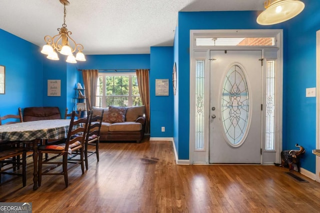 foyer with dark wood-type flooring, a textured ceiling, and a chandelier