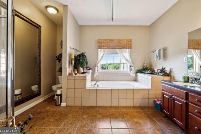 bathroom featuring tile patterned flooring, vanity, tiled bath, a textured ceiling, and toilet